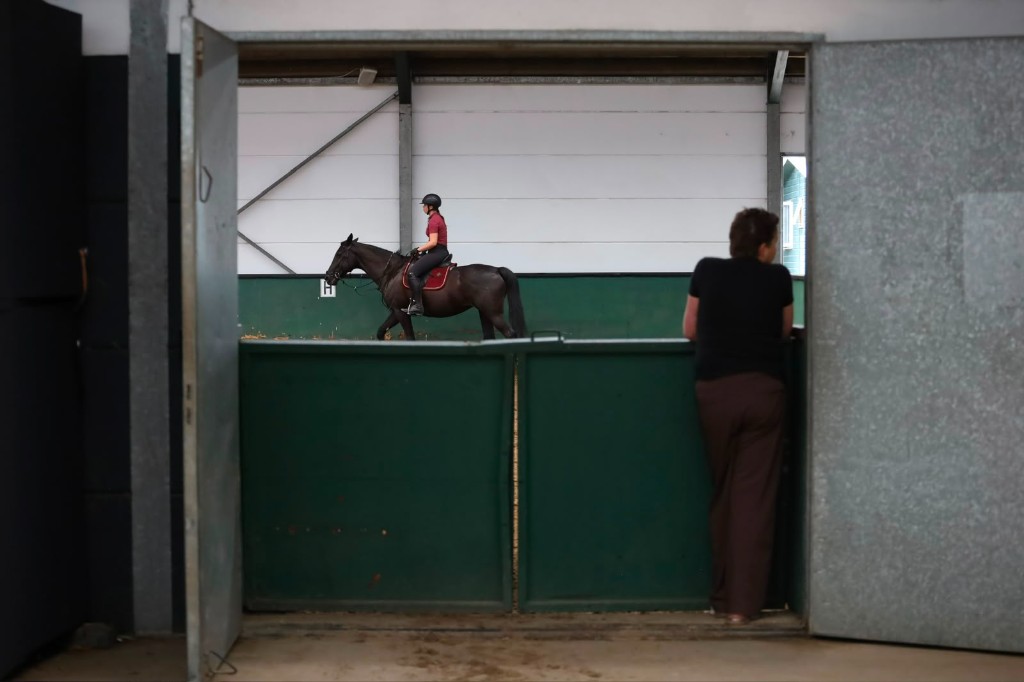 Ruiter op een donker paard in de binnenbak, gezien door de deuropening met een toeschouwer
